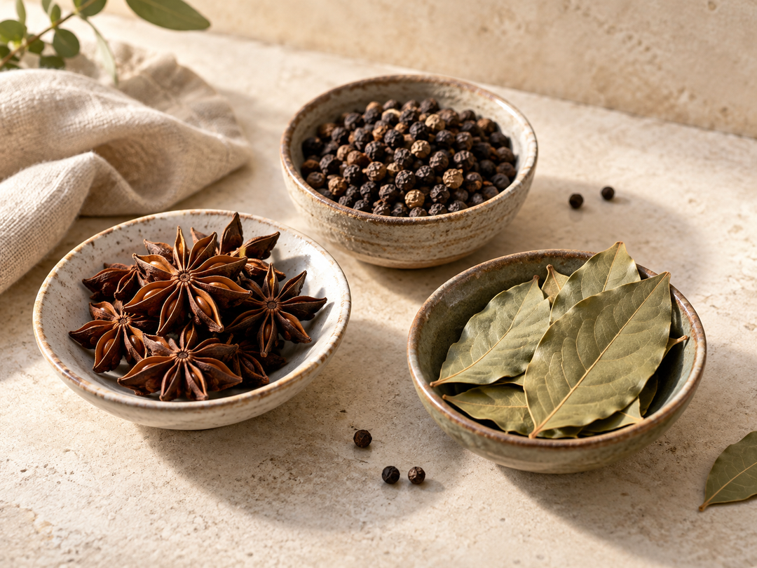 Editorial illustration: Three small ceramic dishes with whole star anise, black peppercorns and dried bay leaves.