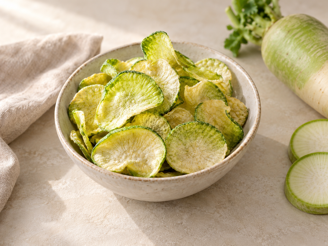 Editorial illustration: A small bowl of crisp vacuum-fried pale green radish chips, thin irregular slices with natural vegetable texture.