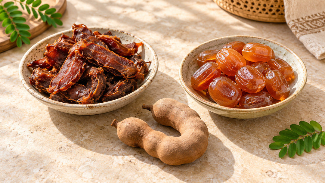 Two ceramic bowls showing dried tamarind pieces and amber tamarind candies with whole pods on stone
