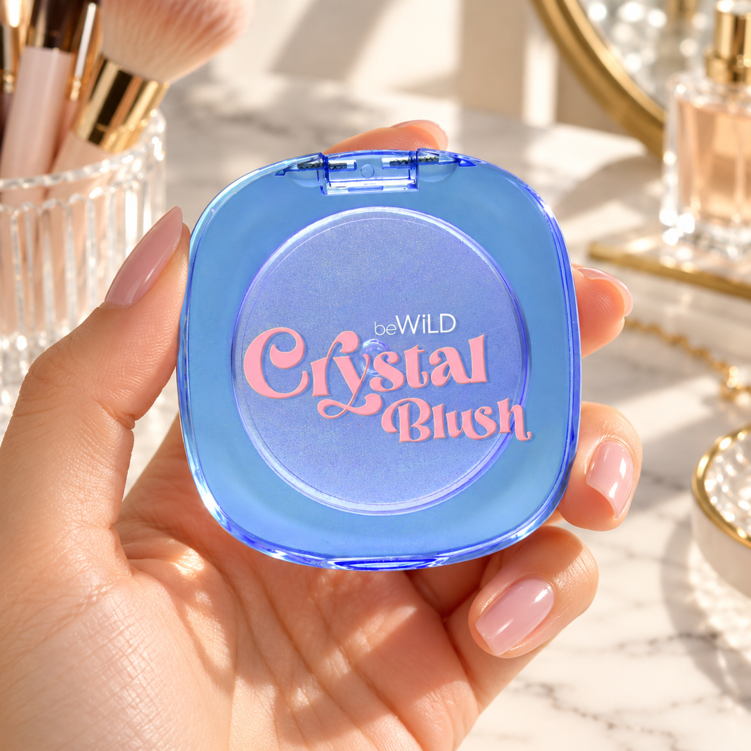 beWiLD Crystal Blush, shade Crystal, held in a hand at a beauty vanity