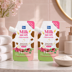 Two Yoko Milk Spa Salt Niacinamide 350 g body scrub pouches in a pink bathroom spa setting